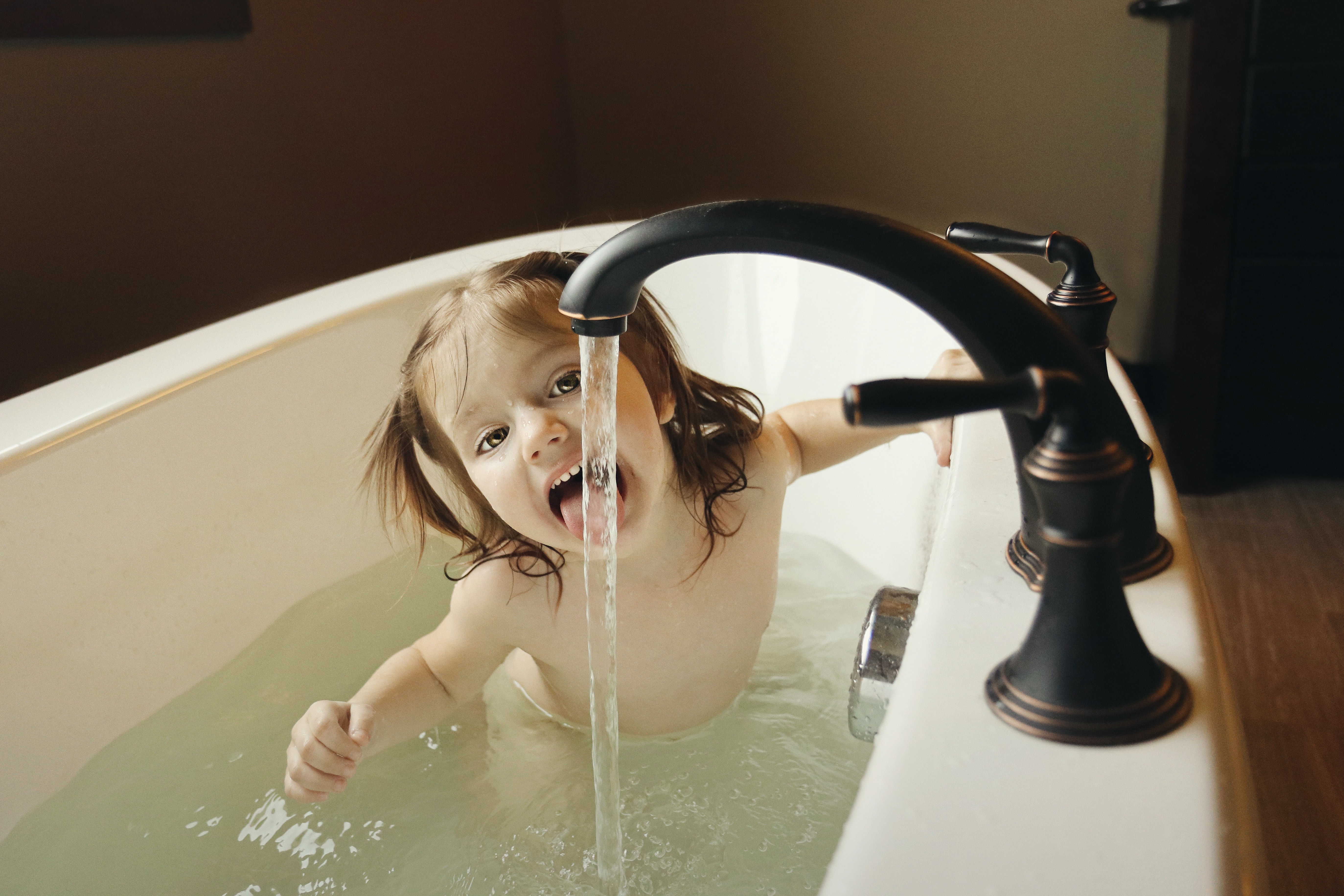  A young child taking a bath and tasting water from the tap